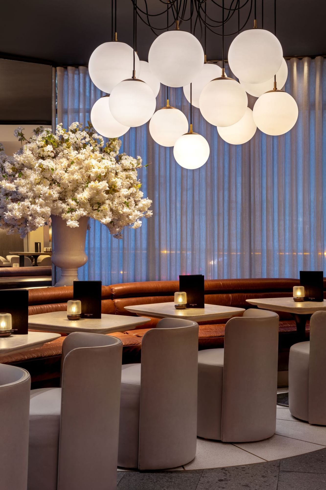 Modern dining area with white chairs, flower arrangement, and globe lights at The May Fair Bar