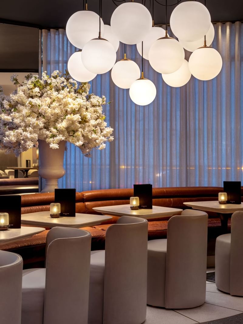 Modern dining area with white chairs, flower arrangement, and globe lights at The May Fair Bar