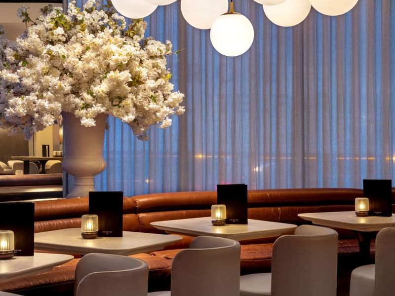 Modern dining area with white chairs, flower arrangement, and globe lights at The May Fair Bar