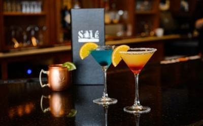 Craft cocktails lined up on a dark wooden bar counter in Solé On The Green at Clemson University Conference Center & Inn