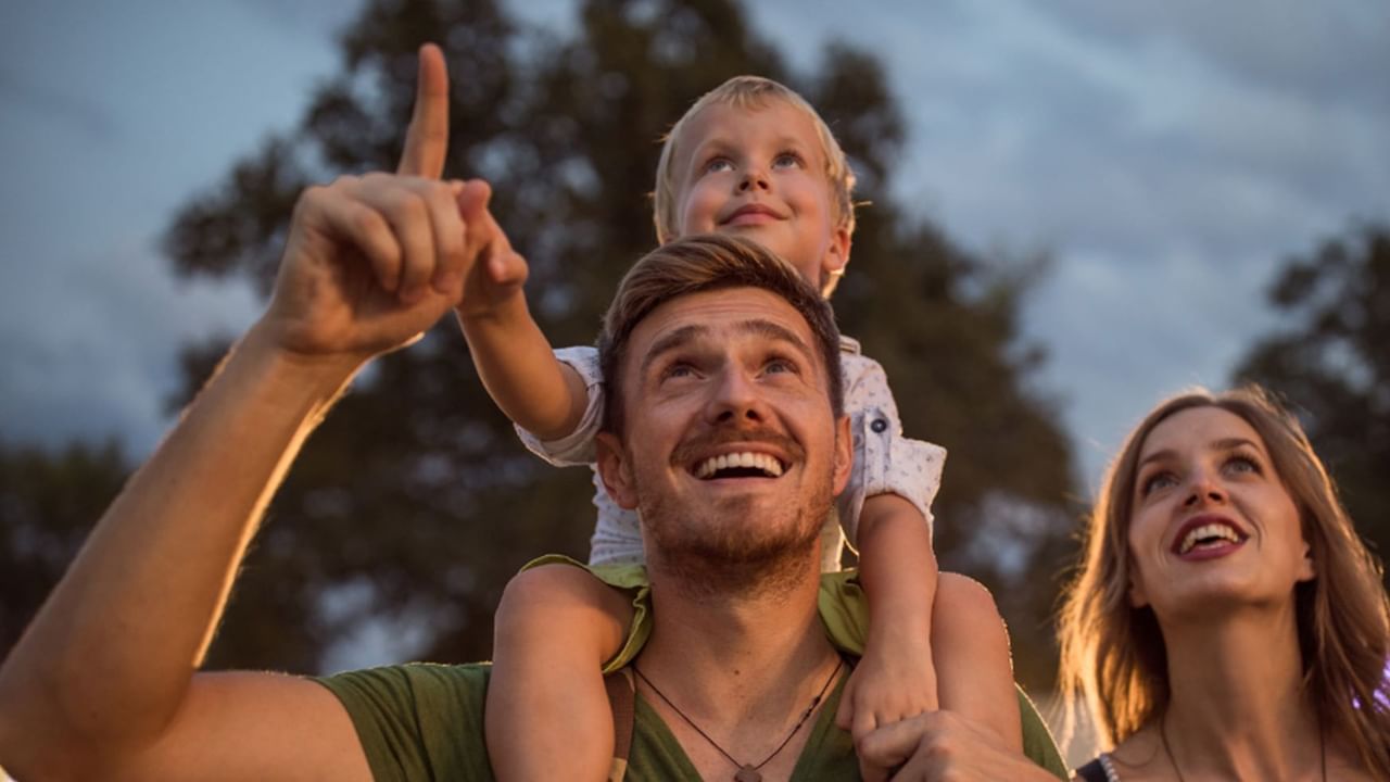 dad with a child on his shoulders and wife beside him looking and pointing up