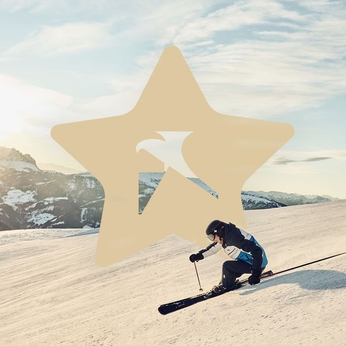 Skier in action on snowy slope with a large star and logo overlay in the background.