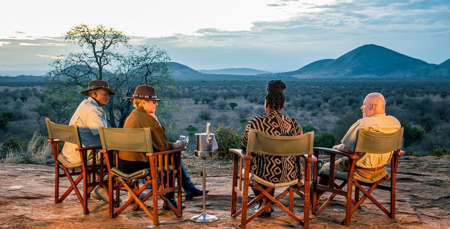 Four people sit on a rocky ledge enjoying sundowners, showcasing eco friendly resort at Serena Hotels & Resorts