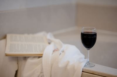 Glass of red wine beside an open book and white folded bathrobe on bathtub edge at La Tourelle Hotel and Spa