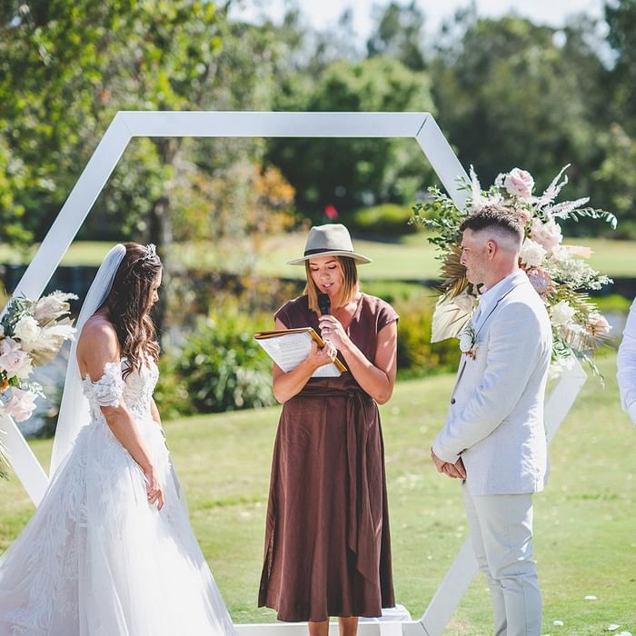 A wedding ceremony with a bride and groom standing by a hexagon arch at Mercure Kooindah Waters