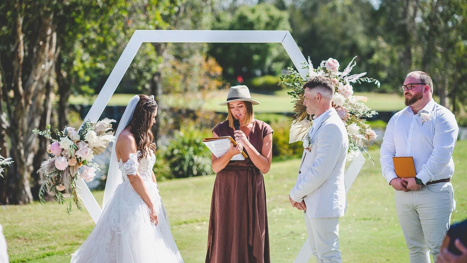 A wedding ceremony with a bride and groom standing by a hexagon arch at Mercure Kooindah Waters