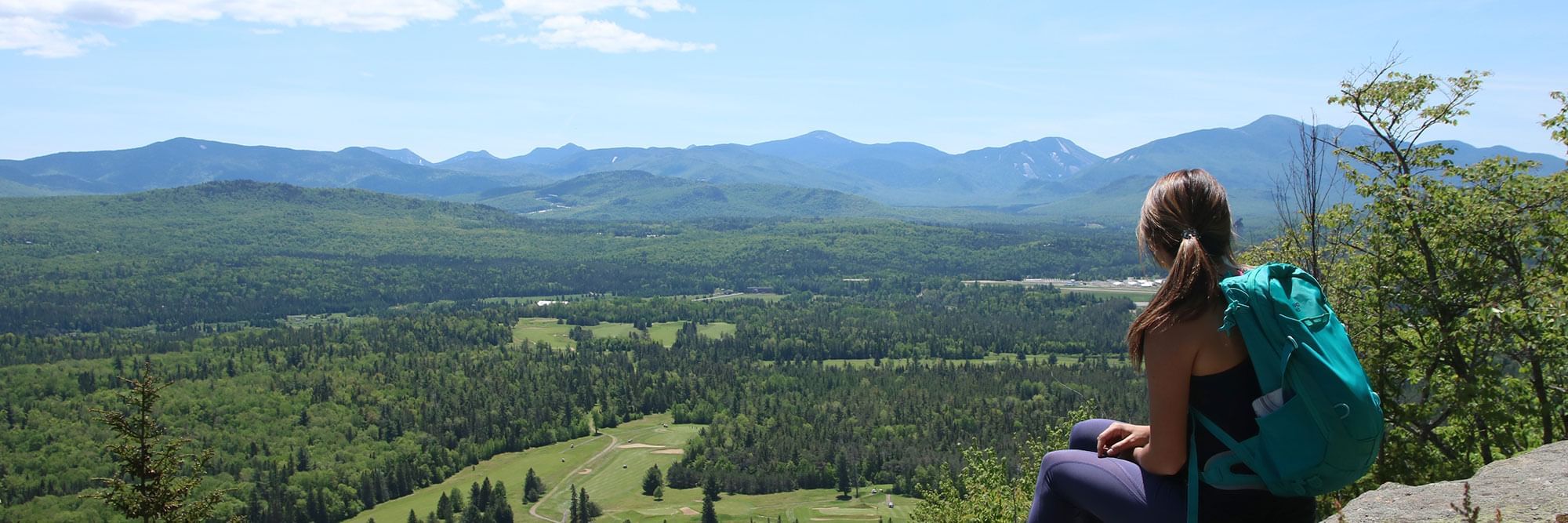 Women sitting on a mountain summit overlooking the Adirondack landscape.