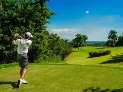 Golfer swinging on the course at Caymanas Golf Club near the Jamaica Pegasus Hotel, surrounded by lush greenery