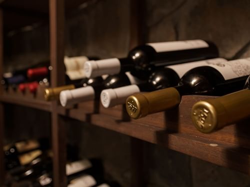 Estante de botellas de vino tinto con tapas blancas y doradas en una bodega en La Cava de Santiago en Hacienda del Mar Los Cabos