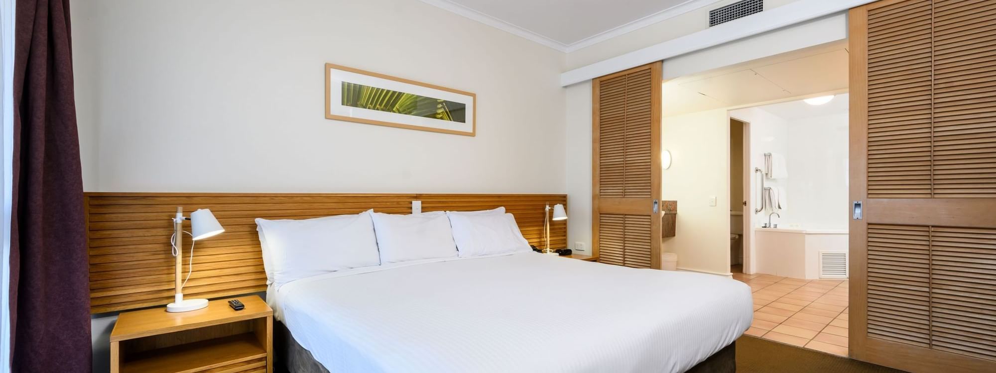 Bed with nightlamps by bathroom vanity in One & Two-Bedroom Suites at Novotel Sunshine Coast Resort
