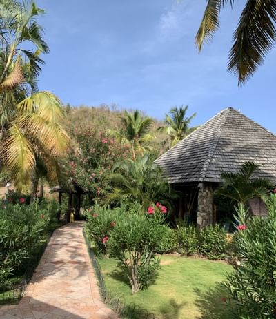 Stone and timber guest hut along a stone path with palm trees and pink flowers at Emerald Beach Resort
