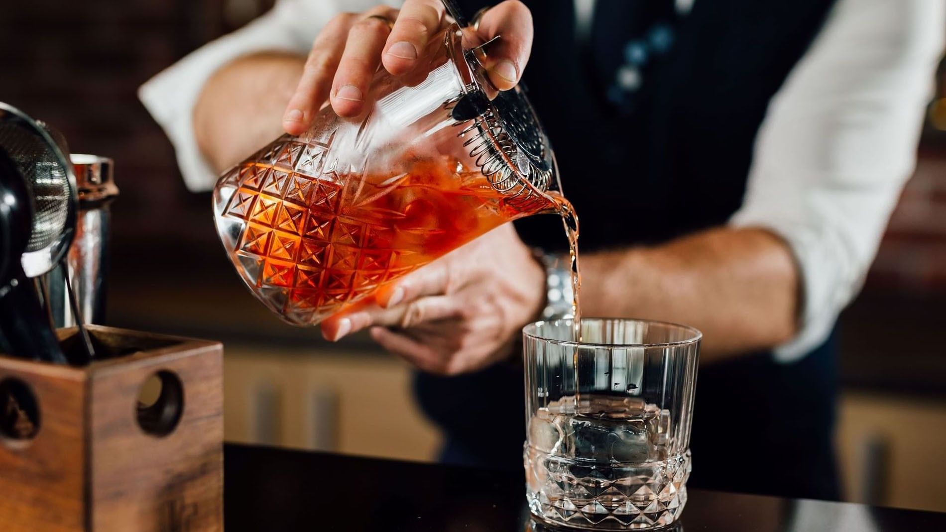 Bartender pouring a cocktail from a glass pitcher into a tumbler by a wooden box in Téséo Bar at Warwick Geneva