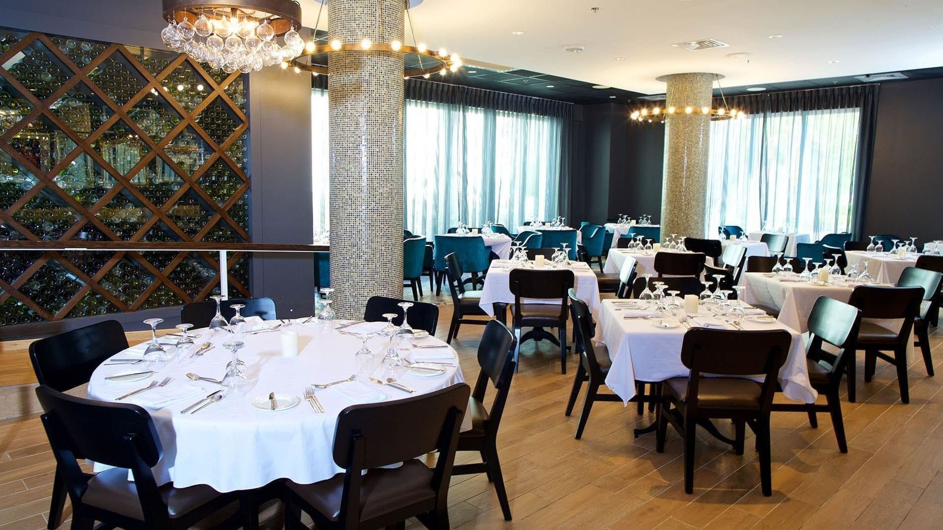 Tables with white cloths by mosaic pillars under ring chandeliers in Abbiocco at Warwick Paradise Island Bahamas