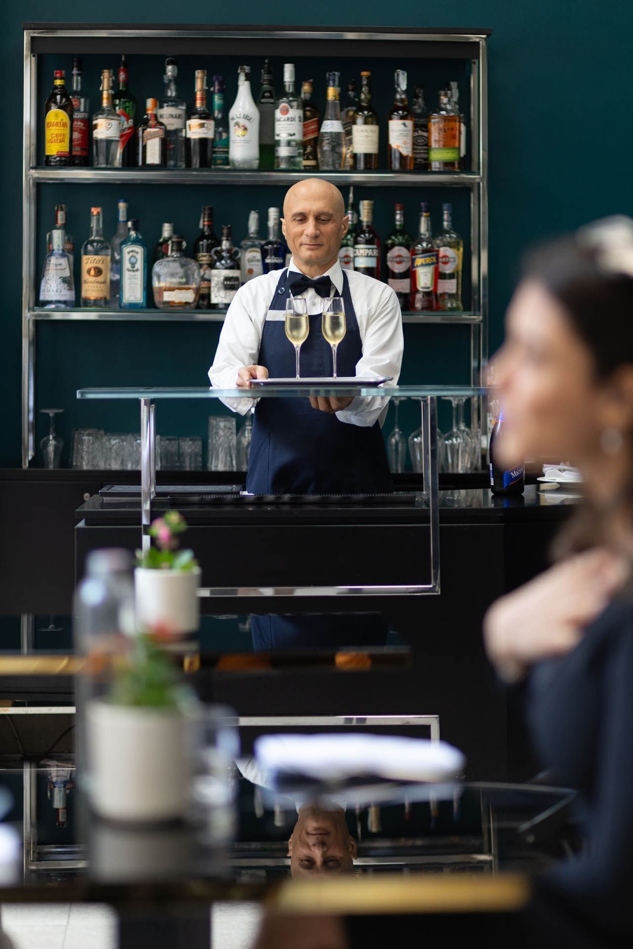A bartender holds a tray with two champagne flutes in a stylish restaurant at The Guardian Hotel