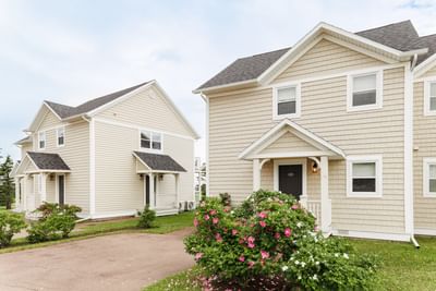Exterior of beige Prince Edward Island cottages with pink flowers at Rodd Crowbush Golf & Beach Resort