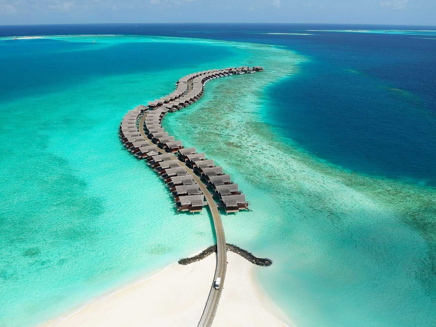 Overwater Grand Park Kodhipparu, Maldives on a curving pier in a tropical blue sea