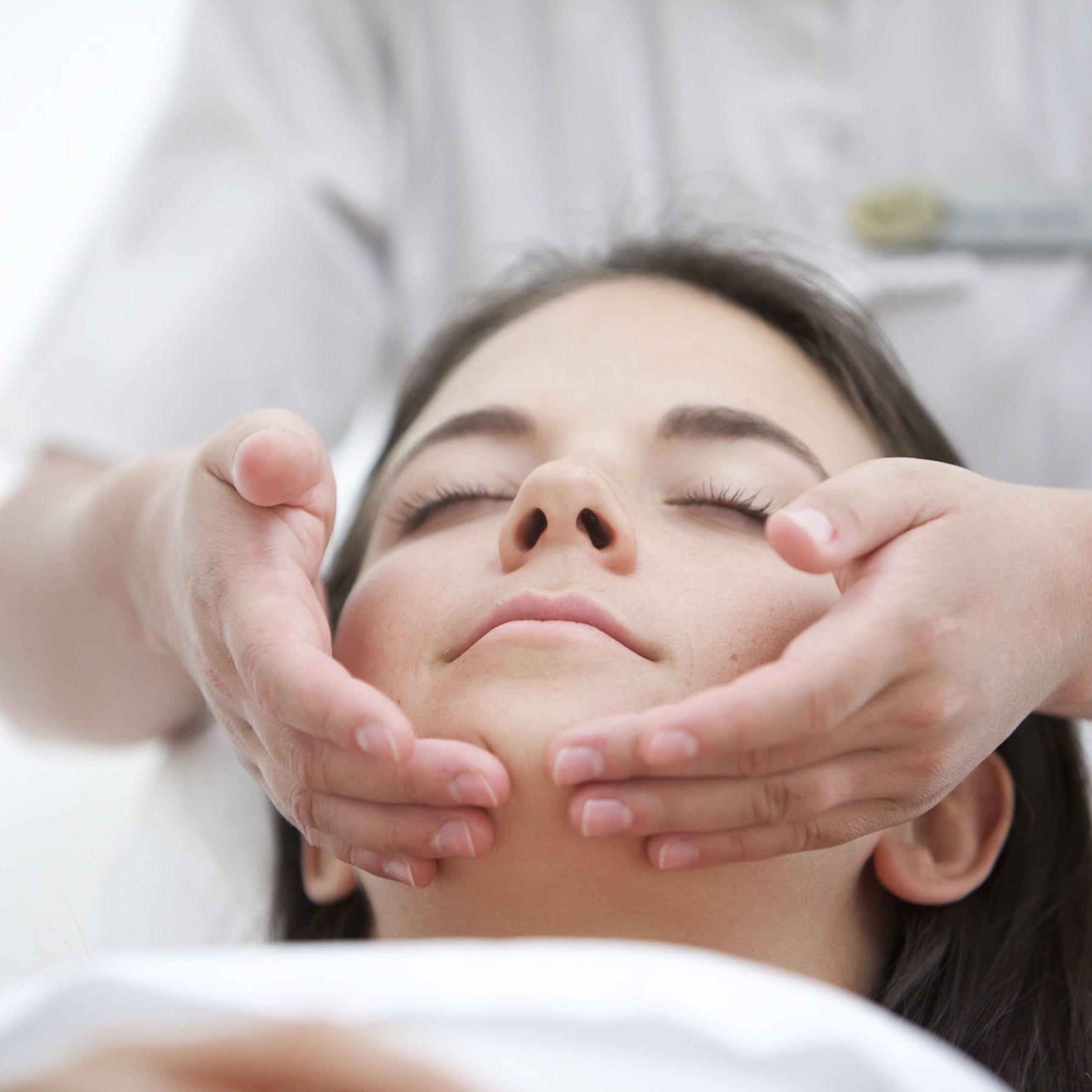 A woman receives a facial massage with hands on her forehead and cheeks, eyes closed.