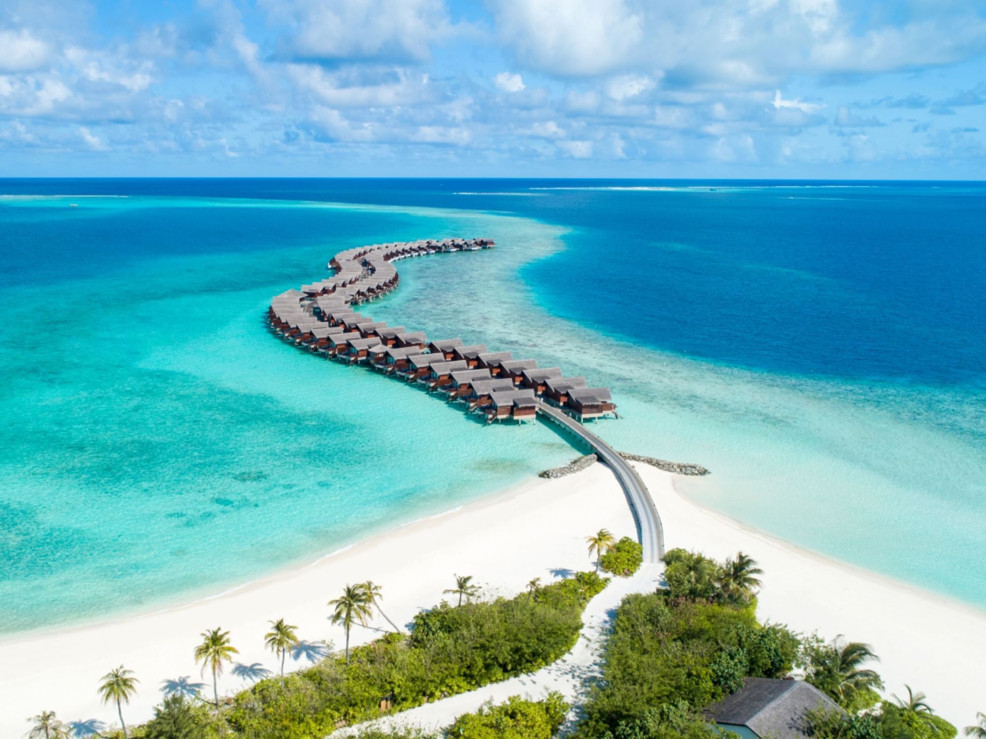 Overwater Grand Park Kodhipparu, Maldives on a curving pier in a tropical blue sea