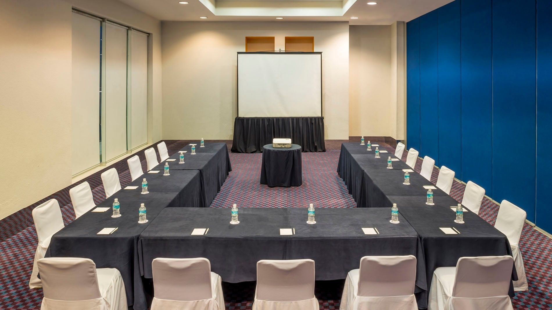 U-shaped Salón Camino Real meeting setup featuring navy linens and a large projector screen at Camino Real Veracruz