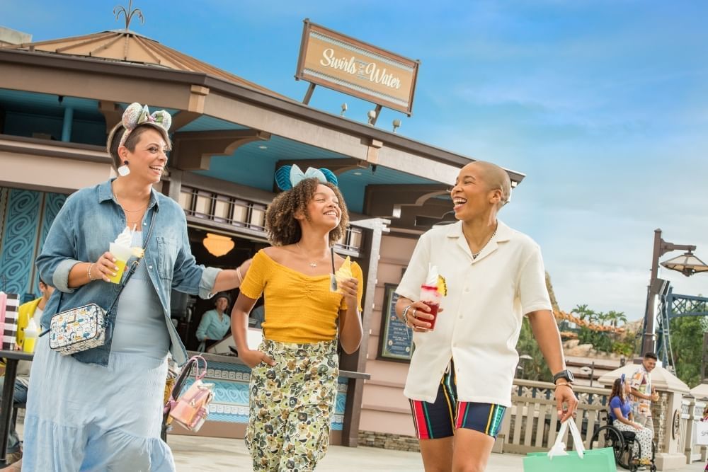 Two women and a girl carry ice cream, smiling and walking away from a building with a sign that reads 