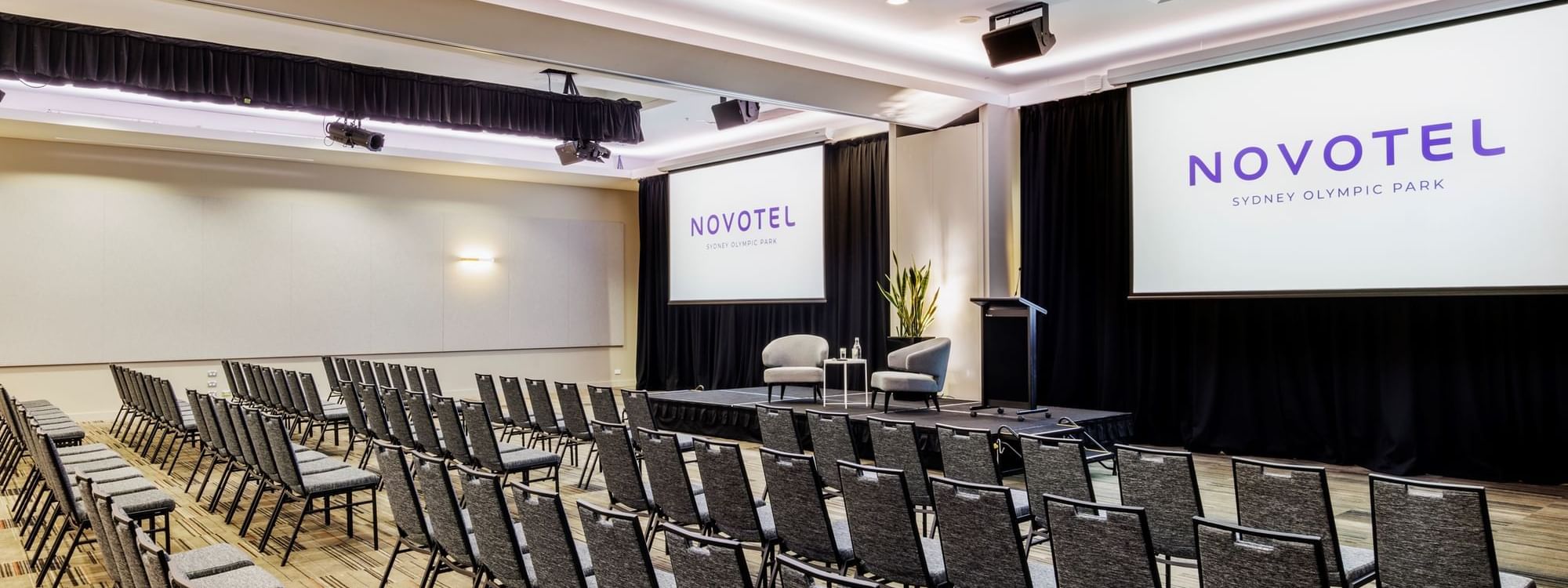 Theatre set-up with projector screens and carpeted floors in Freshwater Ballroom at Novotel Sydney Olympic Park