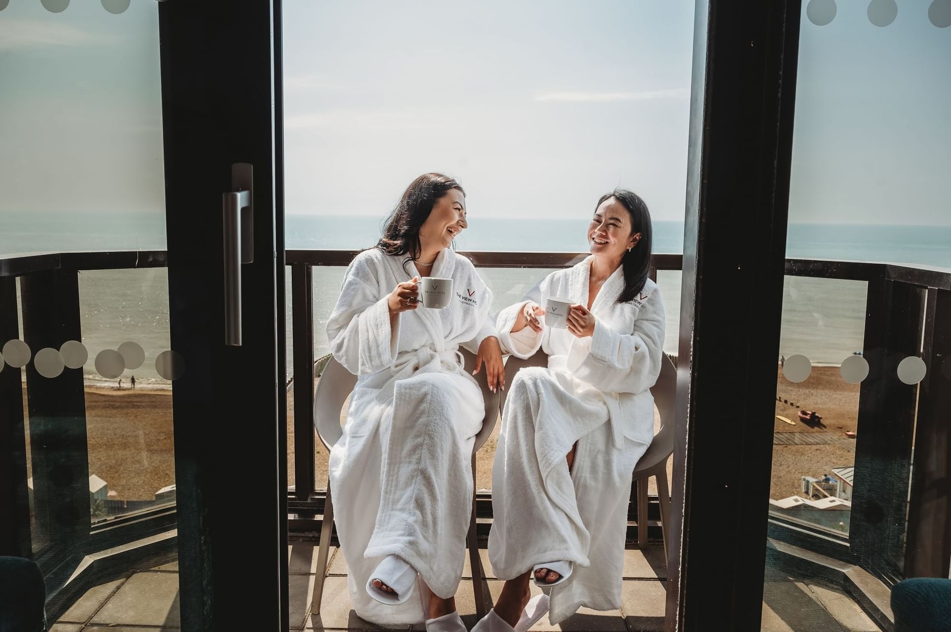 Two women in robes drinking coffee on a balcony overlooking the sea at The View Hotel Eastbourne