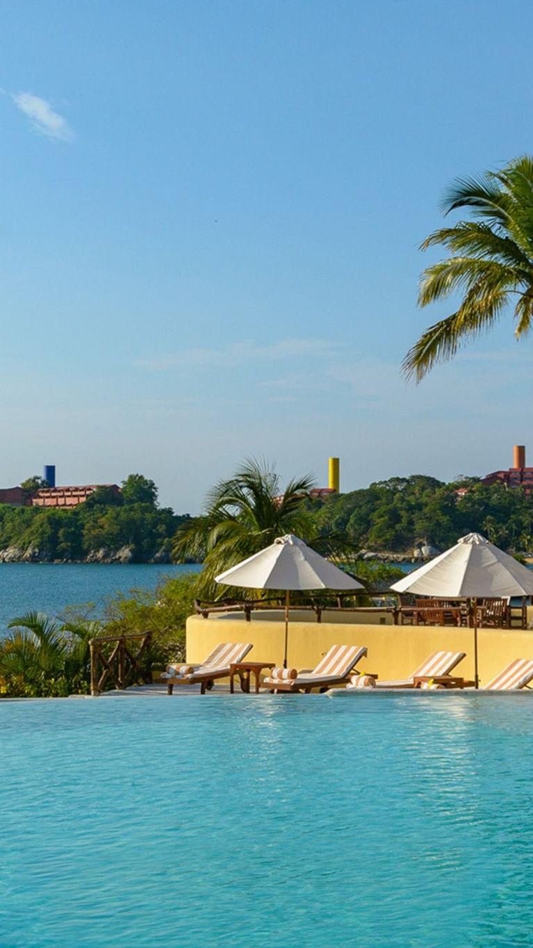 Aerial view of Quinta Real Huatulco featuring white domes by a pool surrounded by thatched roofs at the coast