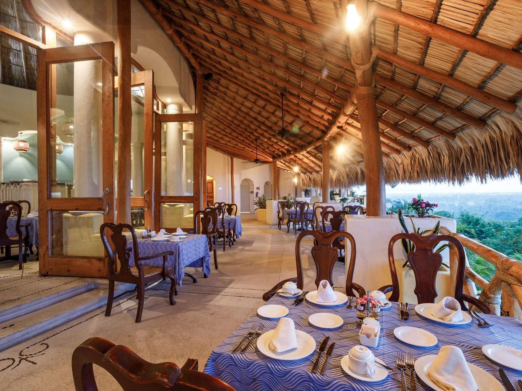 Outdoor dining in Tierra Mia with blue-clothed tables under a large, traditional palapa roof at Quinta Real Acapulco