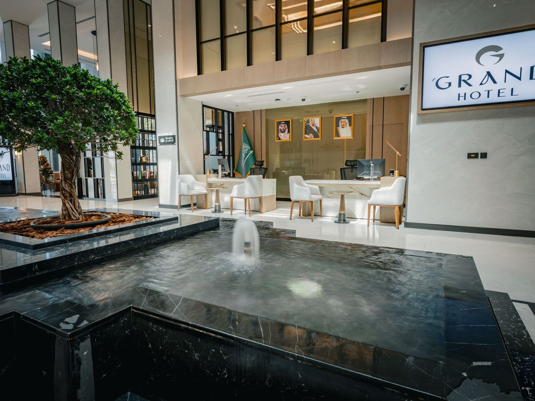 Grand Hotel lobby with a central water feature, white furniture, and framed pictures on the wall.