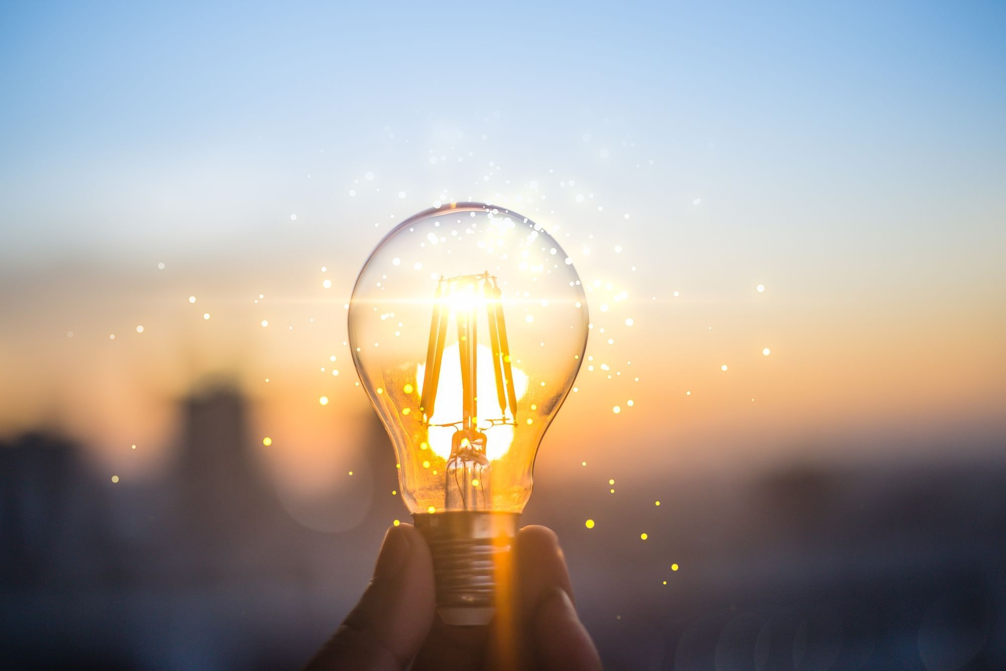 Hand holding a lit bulb against a sunset sky at Warwick Hotels and Resorts