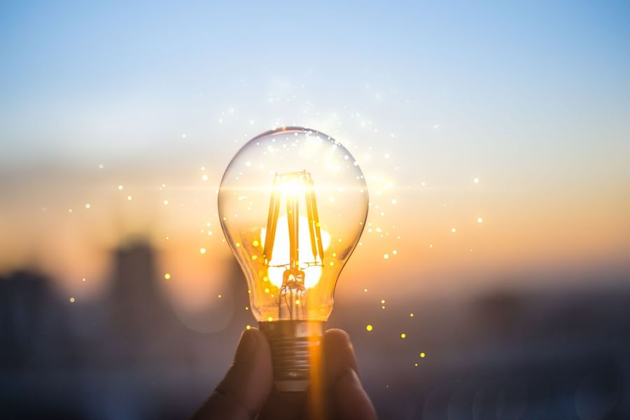 Hand holding a glowing light bulb against a cityscape backdrop image used at Warwick Corporate