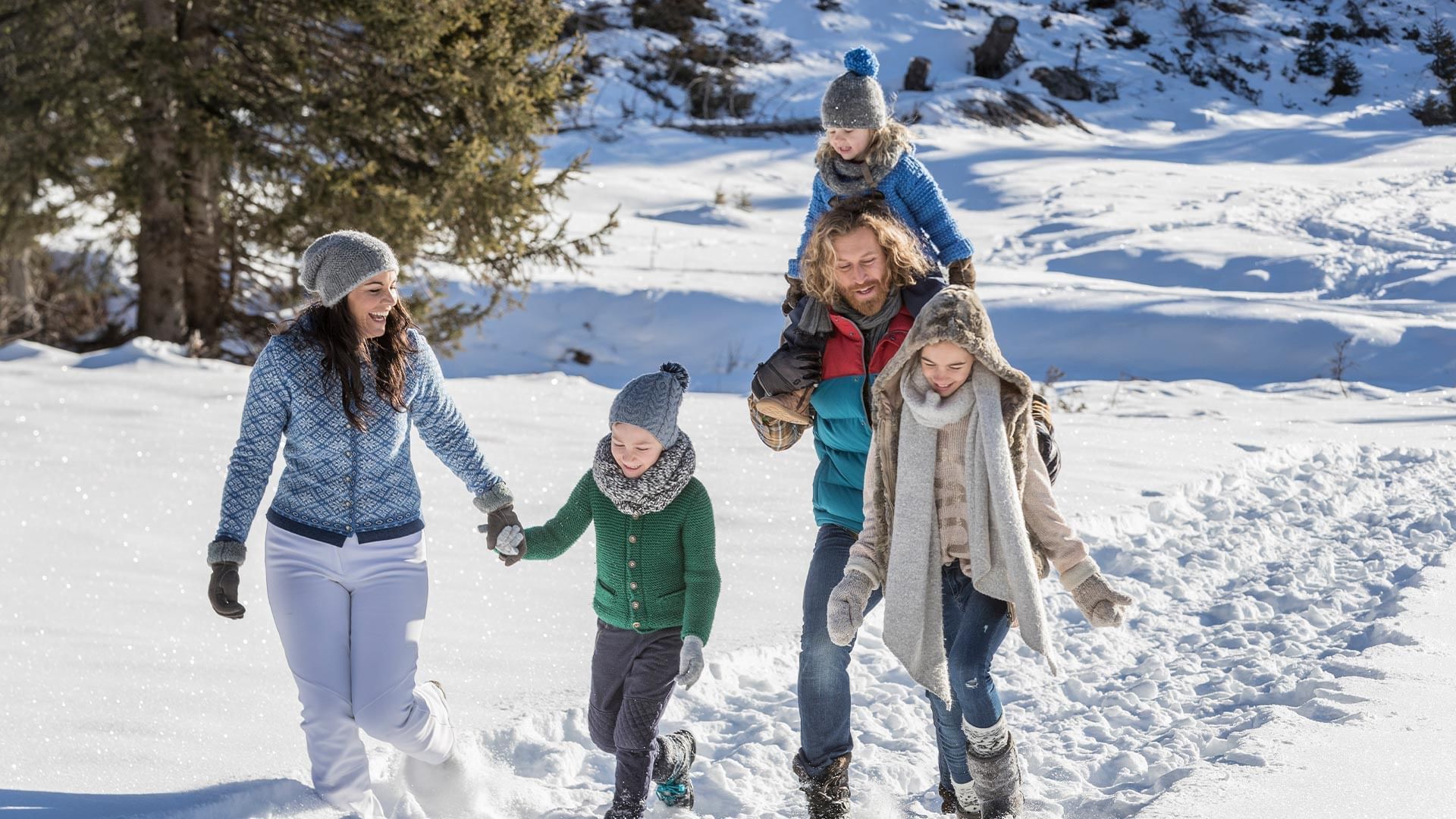 Famiglia felice che cammina insieme nella neve, con un bambino sulle spalle di un uomo.