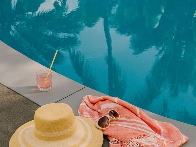 Sun hat, sunglasses, towel, and a cocktail by the beautiful outdoor blue pool at the Kenmore Village Hotel South Beach