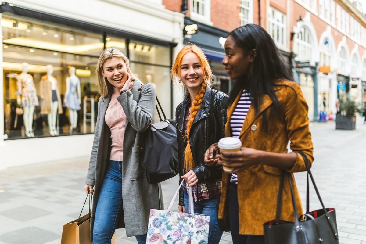 Three friends walking with shopping bags by a storefront near The Capital Hotel, Apartments and Townhouse