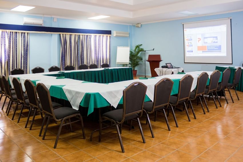 Begonia Conference Room with U-shaped table, chairs, a projector screen, and a podium at Bay Gardens Hotels and Resorts