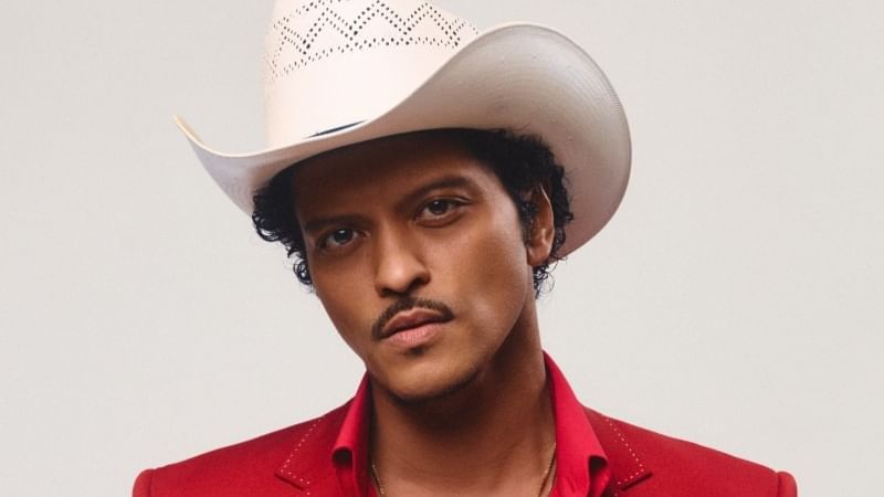 Man wearing white cowboy hat and red embellished suit jacket against neutral background for Bruno Mars The Romantic Tour 2027