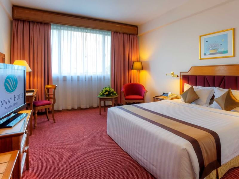Deluxe King room at Sunway Hotel Phnom Penh with a king bed, a red armchair, and a television displaying the hotel's logo