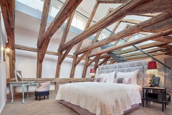 Cozy double bed and dressing table in room with high ceilings supported by old wooden beams in hotel in Vienna