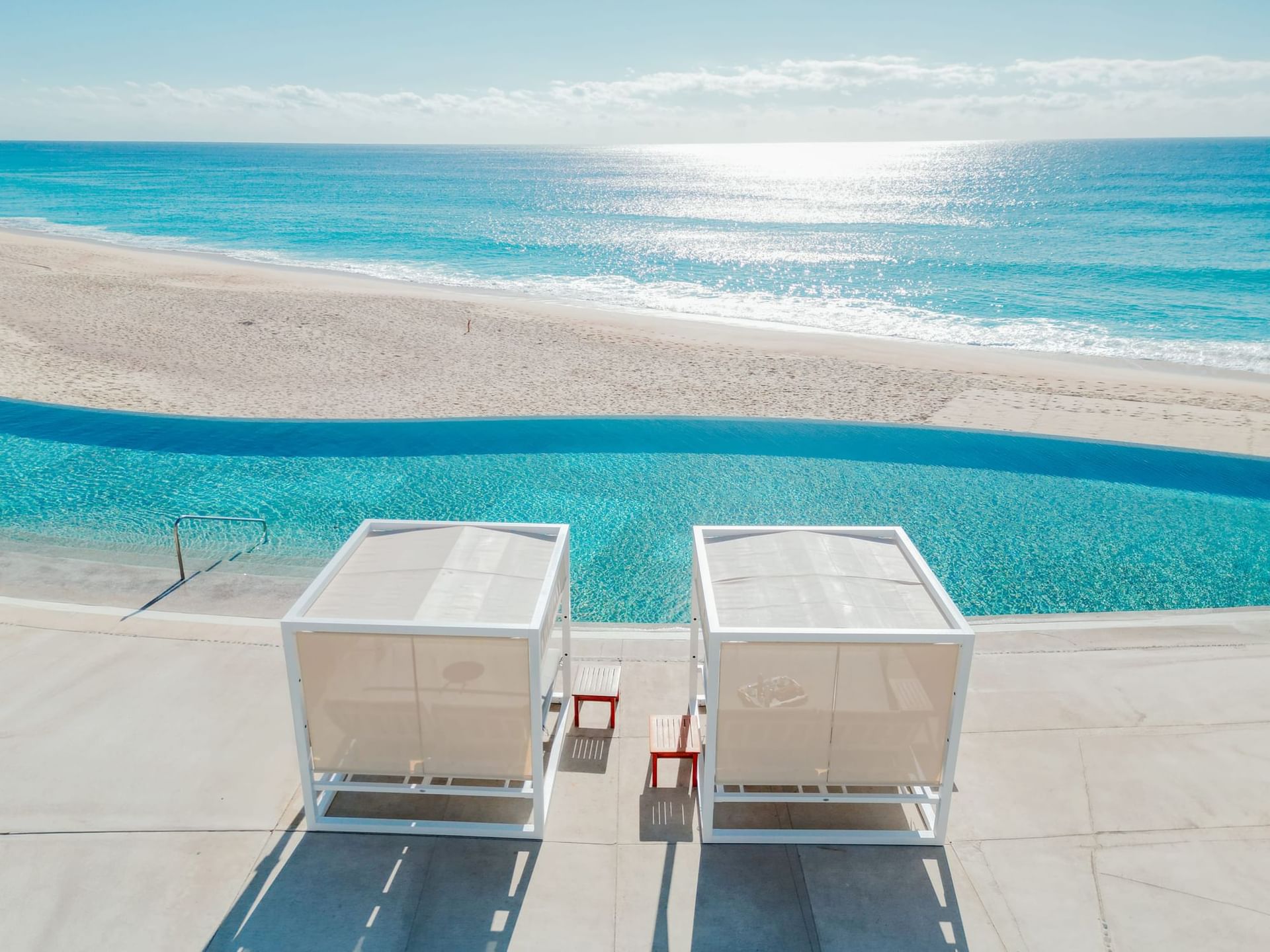 Beachfront infinity pool with private cabanas overlooking the ocean under clear skies at Marquis Los Cabos Resort.