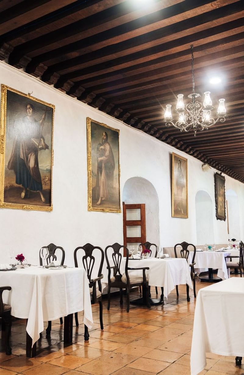 Dining area with white tablecloths, dark wooden chairs, and chandeliers at Quinta Real Oaxaca