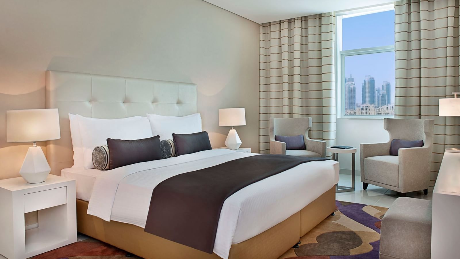 King bed, nightstands & couches with city view in One Bedroom Suite at DAMAC Maison Cour Jardin