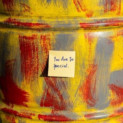 A yellow sticky note reading "You are so special" on a backdrop painted with red, gray, and yellow streaks.