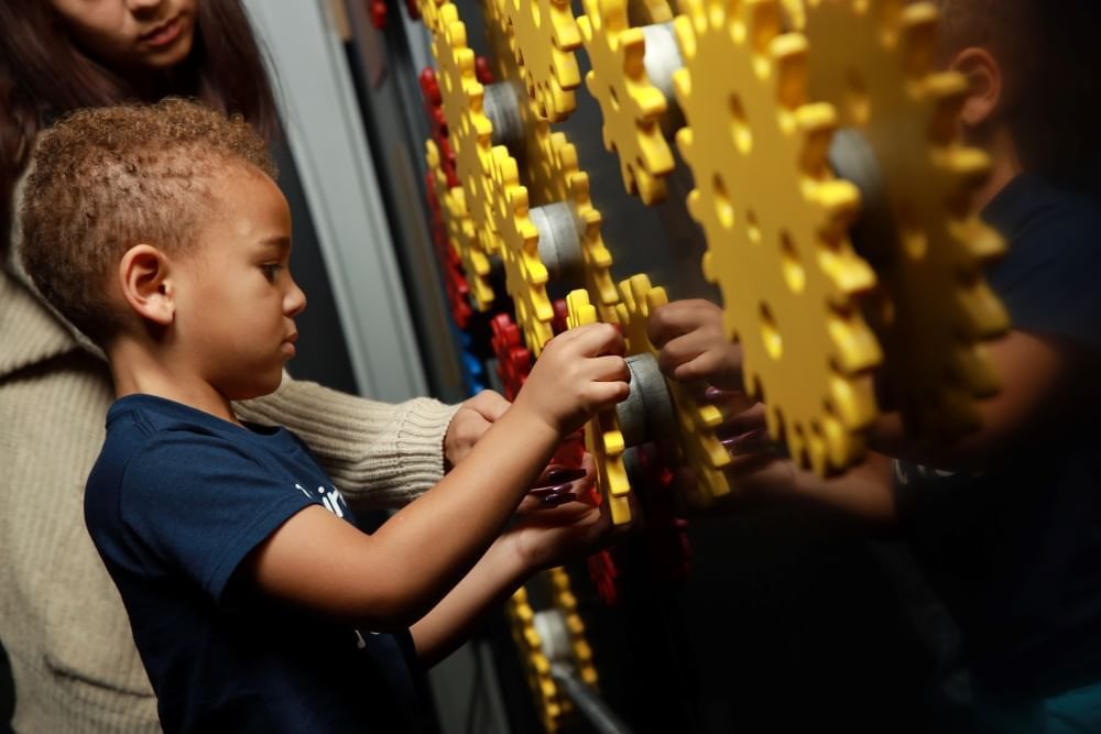 A child interacts with large yellow gears on an interactive wall exhibit at WonderWorks, a great sensory friendly experience in Orlando.