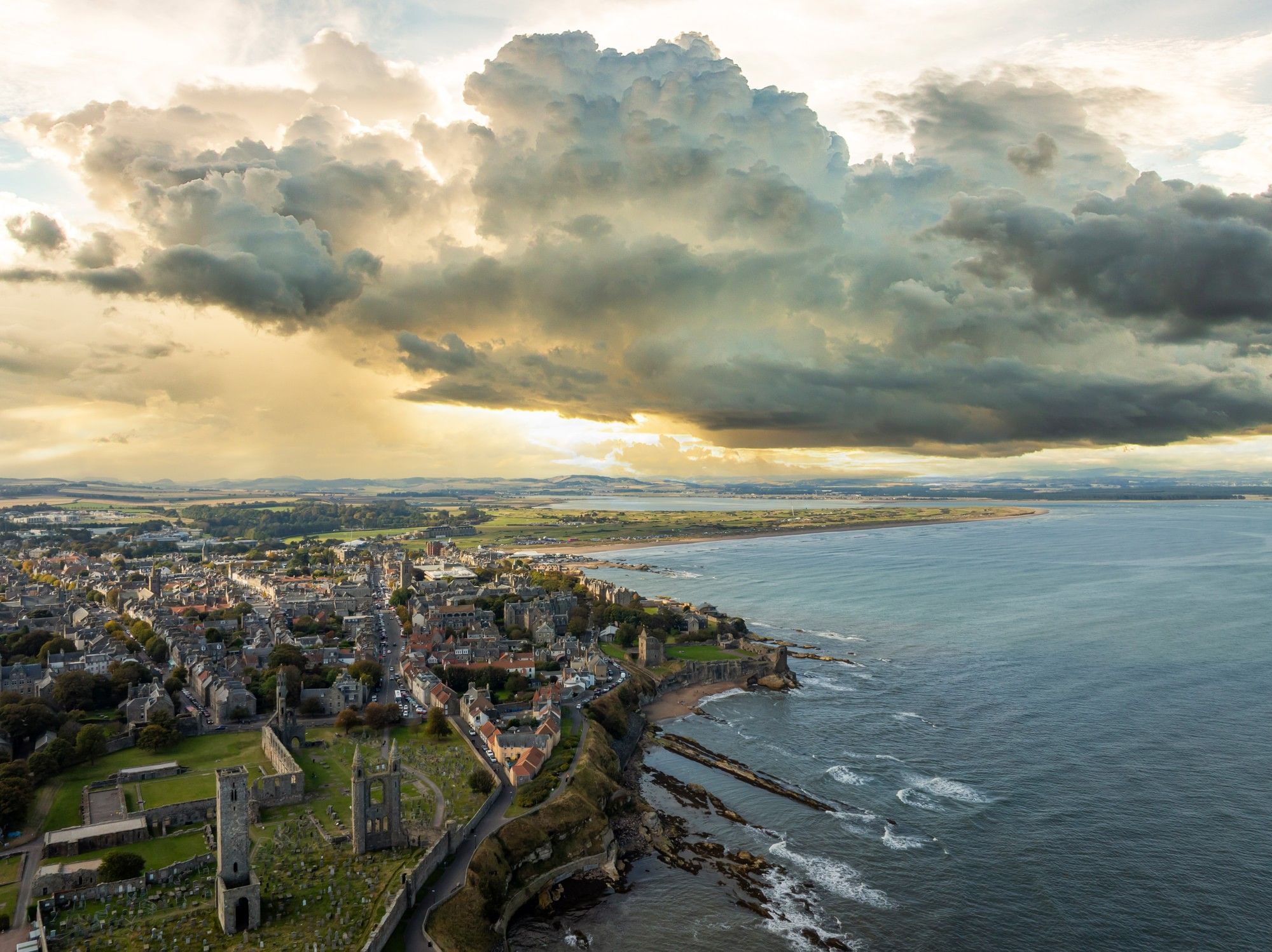 Aerial view of a seaside town with buildings, under a dramatic sky with sunlit clouds near Seaton House