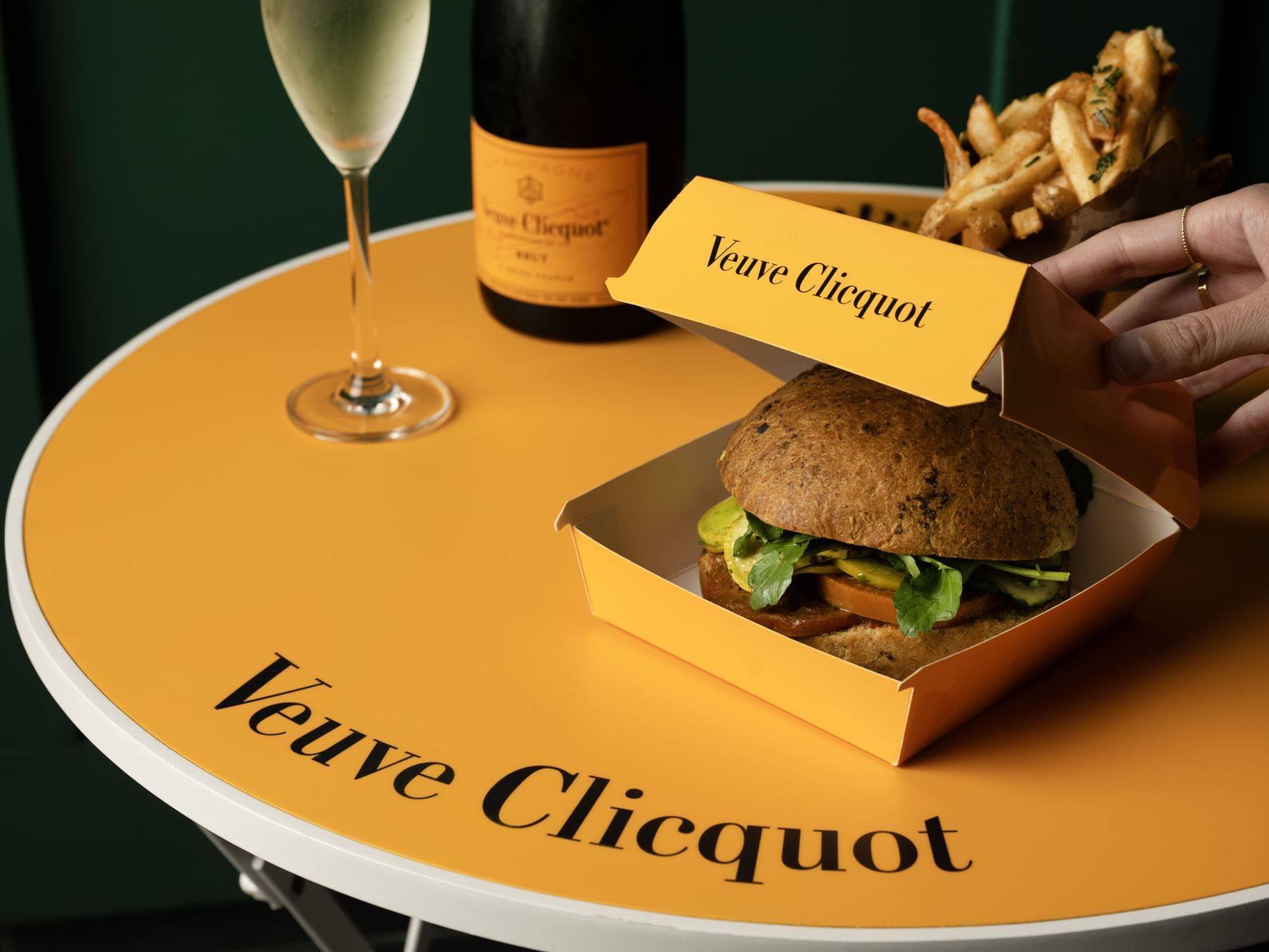 A yellow Veuve Clicquot table with an inspired burger and Veuve Clicquot champagne on it