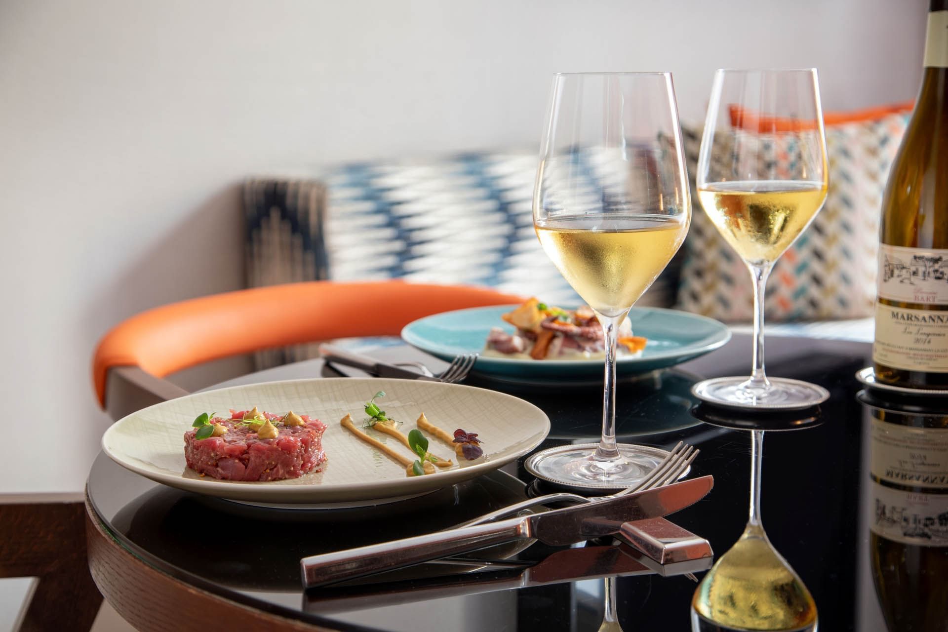 Dining setup with gourmet plates and wine glasses by a colorful sofa in Family Room at The Independent