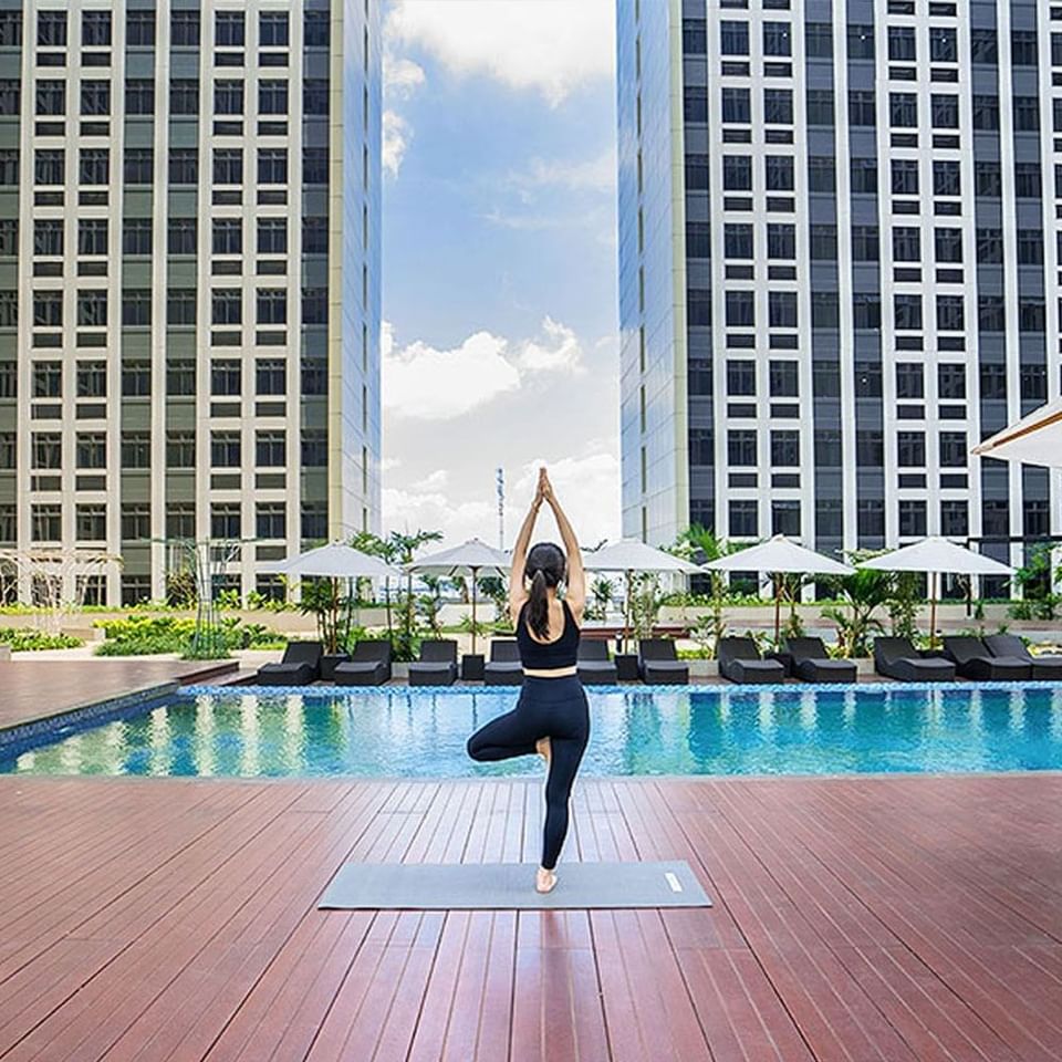 Woman doing yoga on the deck by the pool at LK Cikarang Hotel & Residences