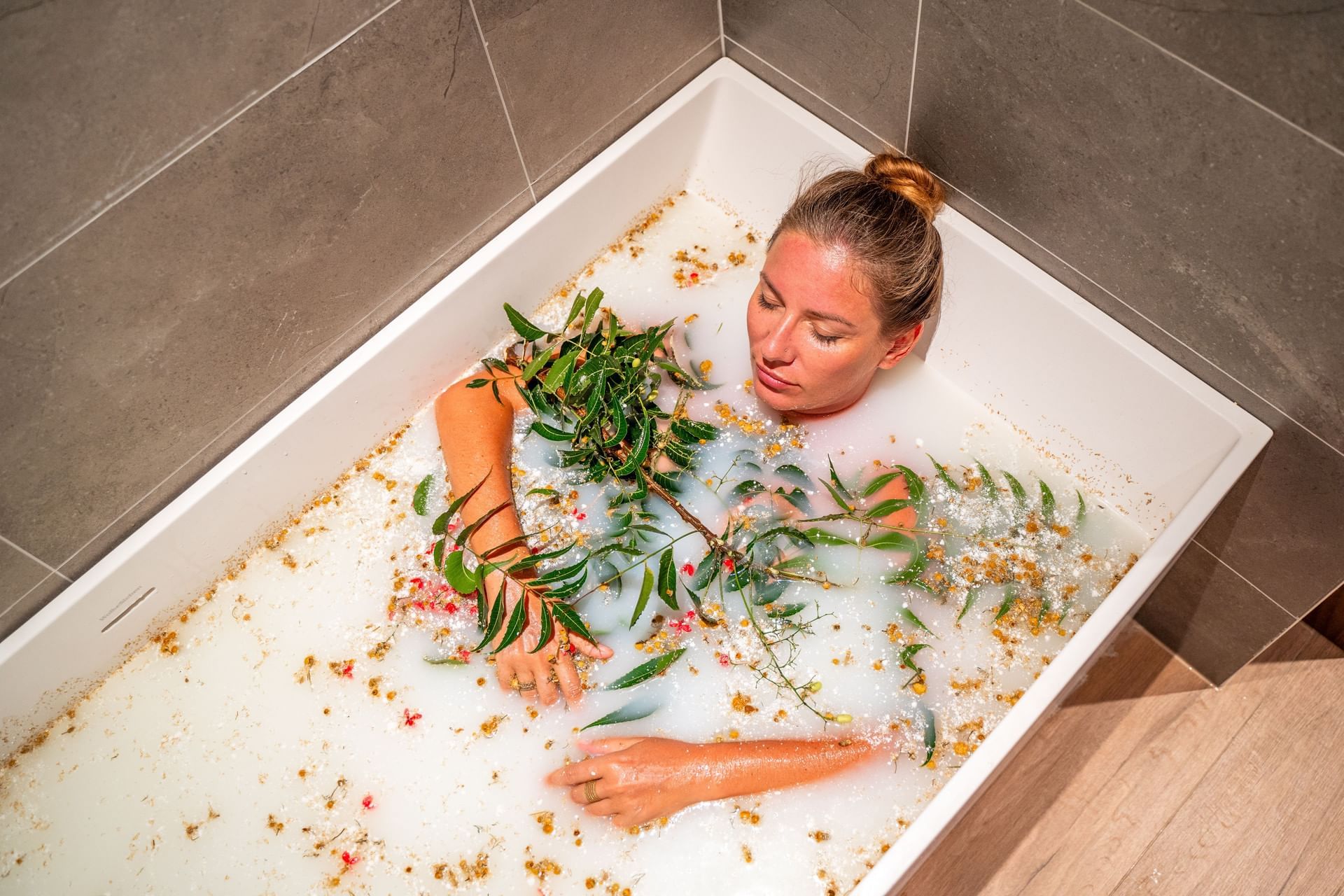 Persoon ontspant in een met bubbels gevuld bad, versierd met groen en bloemblaadjes in The Rock Spa bij Golden Rock Resort