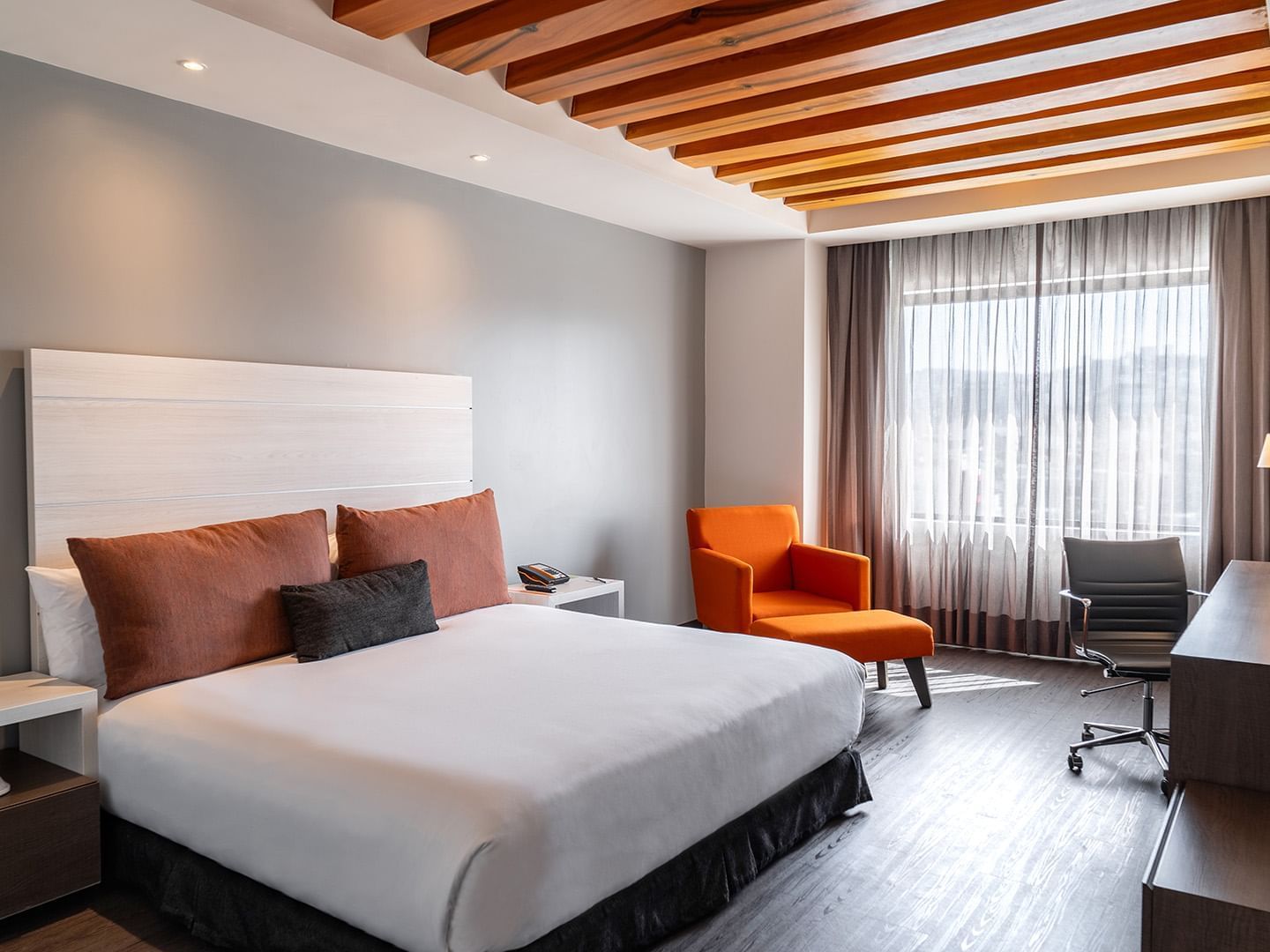 Work desk and cozy lounge chair by the bed in the King Executive Room with wooden floors at Real Inn Tijuana