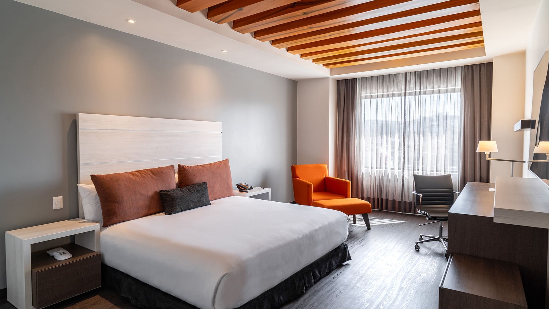 Work desk and cozy lounge chair by the bed in the King Executive Room with wooden floors at Real Inn Tijuana